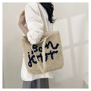Detail of off-white woven tote bag with blue Bon Jour text and braided shoulder strap