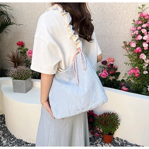 Light blue ruffle shoulder bag with pink drawstring shown on a model in garden