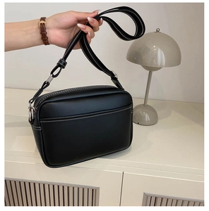 Detail of black PU leather crossbody bag with white contrast stitching and striped strap
