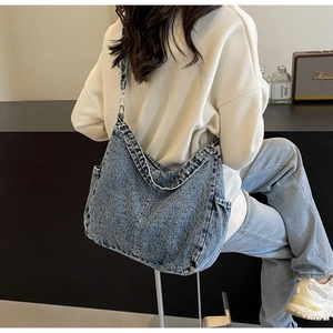 Detail van blauwe denim draagtas met metalen gespen getoond op een vrouwelijk model
