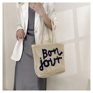 Detail of a beige woven tote bag with Bonjour embroidery shown in a lifestyle scene