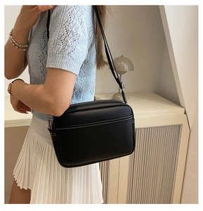 Detail of black PU crossbody bag with white contrast stitching and silver hardware on model