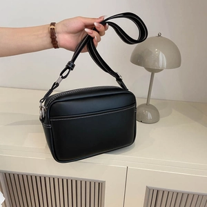Minimalist black camera bag with white stitching and striped wide fabric strap