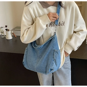 Detail van blauwe denim crossbodytas met handige zijzakken en een zachte gewassen textuur