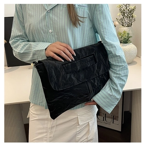 Detail of black pleated textured PU leather clutch bag with glossy finish held by model