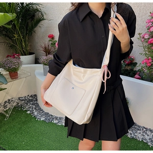 Close-up of cream PU leather crossbody bag featuring pink drawstring bow and front pocket