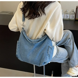 Detail van een grote denim crossbody tas met zijvak en metalen hardware op het model