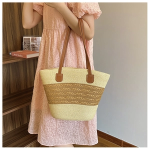 Detail of woven straw tote bag featuring contrast colors and leather handles on a model