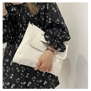 Detail of white PU leather crossbody bag with pleated texture and metal D-ring attachment