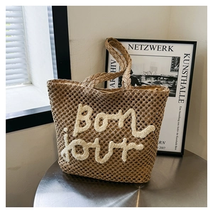 Minimalist hand-woven khaki tote bag with plush Bonjour lettering on metal table