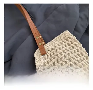 Close-up of woven cream shoulder bag with brown leather strap and gold metal rivets