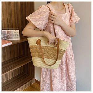 Detail of woven straw tote bag featuring beige and caramel patchwork with leather handles