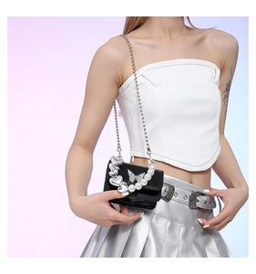 Detail view of black patent leather crossbody bag with pearl heart chain and crystal butterfly