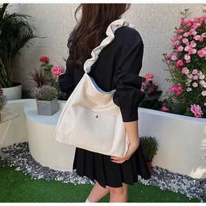 Outdoor shot of cream PU shoulder bag featuring ruffled straps and front pocket detail