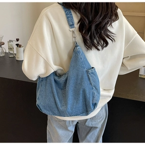 Blauwe denim hobo tas met verstelbare riem gedragen door een model in een café omgeving
