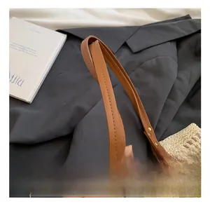 Detail of woven beige handbag featuring brown faux leather handle with metal rivets