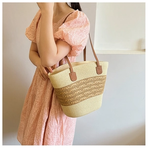 Detail of woven straw tote bag featuring brown leather straps and wavy knit patterns