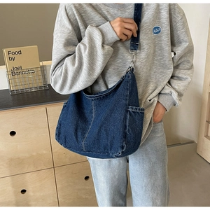 Detail van donkerblauwe denim crossbodytas met witte stiksels en een handig zijvakje