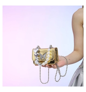 Detail view of mini gold mirror bag with silver heart charms and white pearl handle