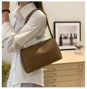 Side view of a brown minimalist faux leather shoulder bag worn by a model in a cozy room