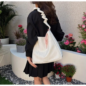 Detail of trendy off-white PU shoulder bag with ruffled strap and pink cord charm