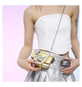 Detail of a metallic gold crossbody bag featuring a crystal butterfly and pearl chain strap