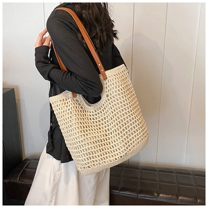 Detail of cream woven tote bag with brown leather shoulder straps and metal rivets