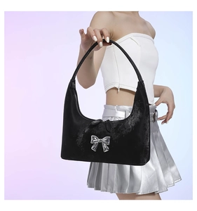Detail view of black velvet handbag with silver bow charm on blue gradient background