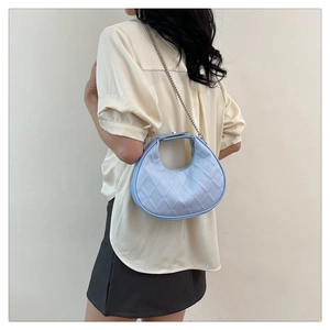 Détail du sac demi-lune matelassé bleu clair avec bandoulière chaîne porté par un mannequin
