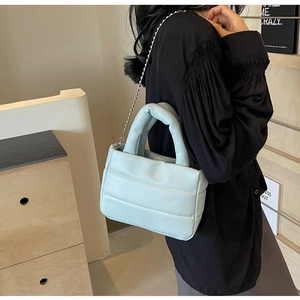 Macro detail of a light blue quilted puffer bucket bag with stylish silver ball chain strap