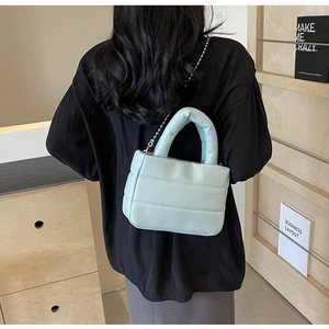Detail of light blue quilted crossbody bag with soft puff texture and thin metal chain