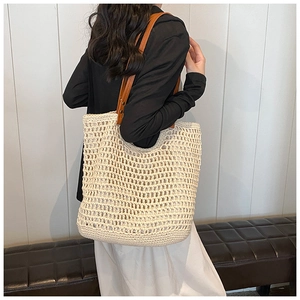 Detail of hand-woven beige tote bag with brown faux leather handles and golden studs