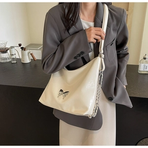 Detail of cream patent leather hobo bag with a silver butterfly buckle and chain strap