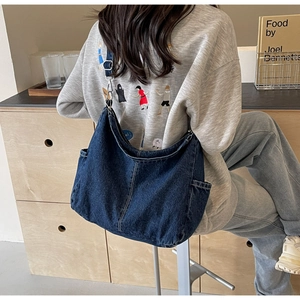 Detail van een grote donkerblauwe denim crossbodytas met een zijvak voor opslag