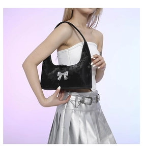 Detail of a black PU leather shoulder bag with a silver metallic bow and Y2K aesthetic style