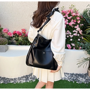 Detail of black PU leather tote bag with pleated wide strap and metal magnetic snap pocket