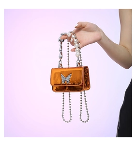 Detail of orange mini PU bag featuring a silver rhinestone butterfly and pearl chain strap