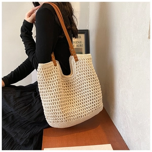 Close-up of woven cream tote bag featuring brown faux leather straps and metal rivets
