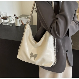Close-up of off-white PU leather bag with silver butterfly buckle and chain on counter