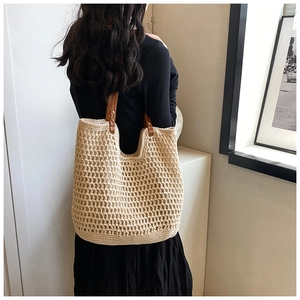 Close-up of woven mesh tote bag featuring brown leather straps and gold metal rivets