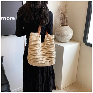 Detail view of woven tote bag with brown leather handles and metal rivet reinforcement