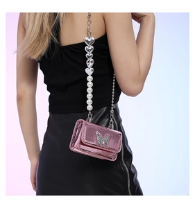 Close-up of pink metallic crossbody bag with silver butterfly logo and pearl heart strap