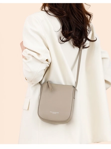 Detailed view of taupe lychee leather crossbody bag on a model in a white blazer