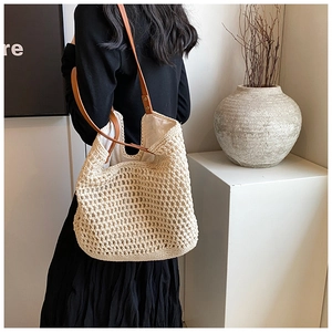 Detail of off-white woven tote bag with brown leather handles and silver rivet accents