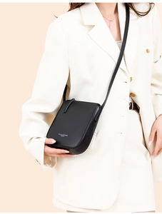 Detail of black pebbled leather crossbody bag with white STLY & LEATHER logo on a model