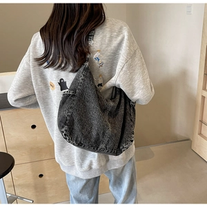 Detailopname van de grote gewassen zwarte denim crossbody draagtas op een model