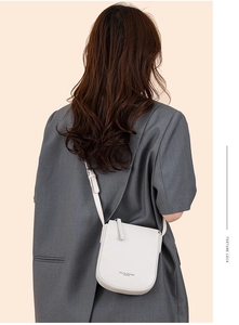 Detail shot of a white leather crossbody bag worn over a gray oversized suit jacket