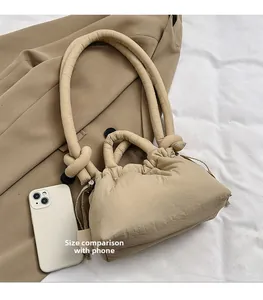 Quilted beige puffer bag detail with knotted handle and size reference to a smartphone