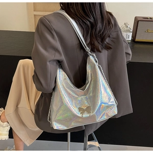 Detail of holographic silver hobo bag featuring a golden butterfly logo and metal chain