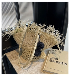 Dettaglio della borsa in paglia beige con lunghe frange e ciondoli a pompon colorati